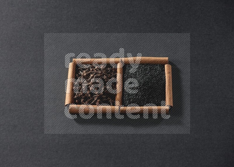 2 squares of cinnamon sticks full of black seeds and cloves on black flooring