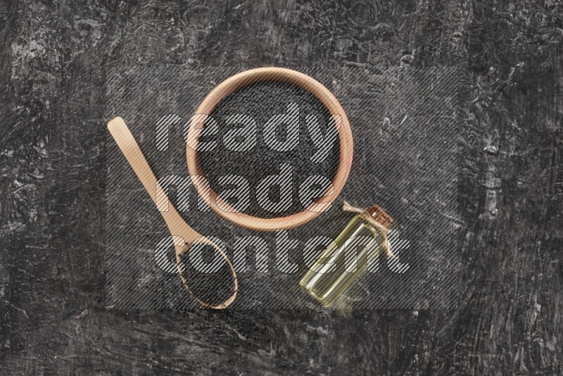 وعاء خشبي وملعقة خشبية ممتلئان ببذور حبة البركة مع زجاجة من زيت حبة البركة علي خلفية سوداء