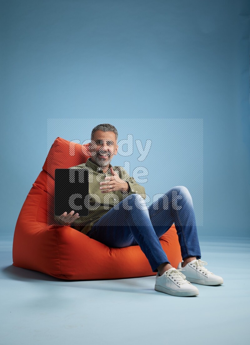 A man sitting on an orange beanbag and working on tablet