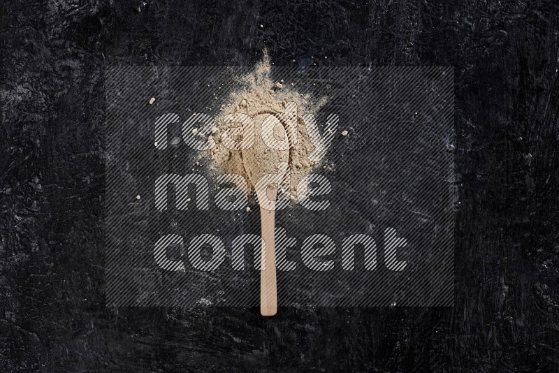 A wooden spoon full of garlic powder surrounded by the powder on a textured black flooring in different angles
