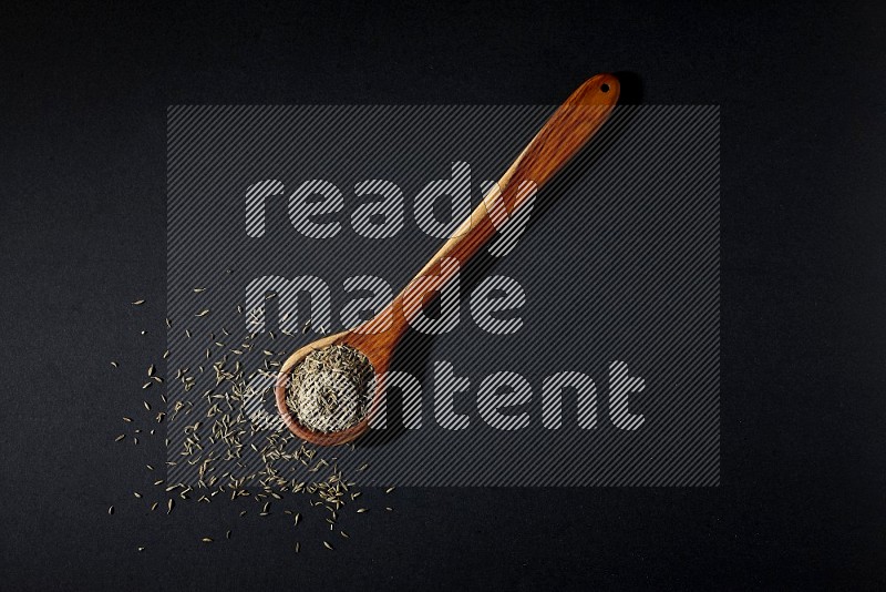 A wooden ladle full of cumin seeds on black flooring