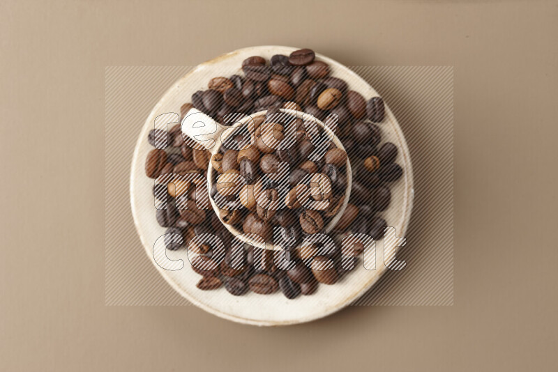 A beige pottery cup full of roasted coffee beans on beige background