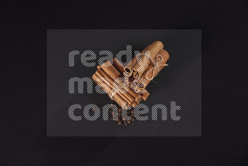 Two bounded stacks of cinnamon sticks with cloves on black background