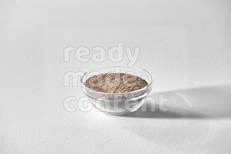 A glass bowl full of black pepper powder on white flooring
