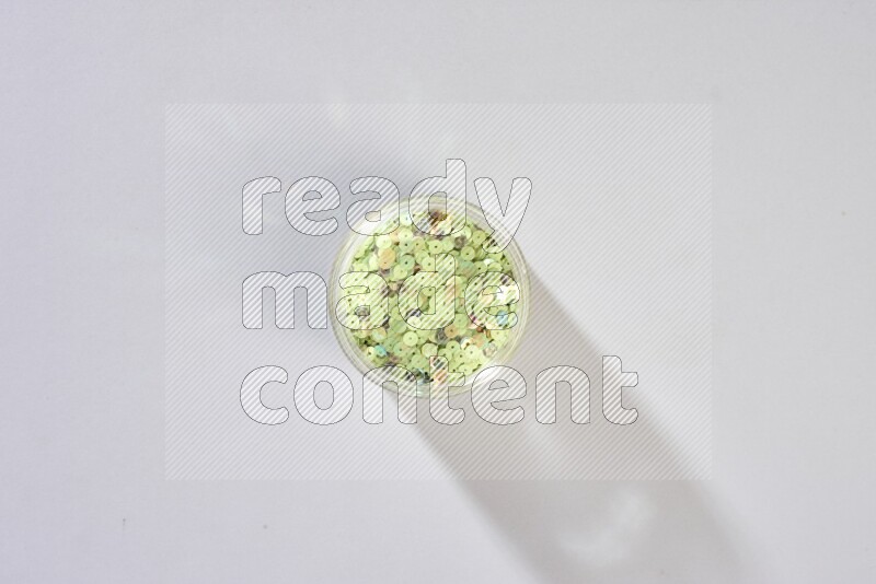 Colored flat sequins in a glass jar on grey background