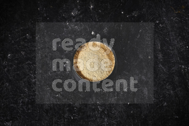 A black pottery bowl full of ground ginger powder on black background