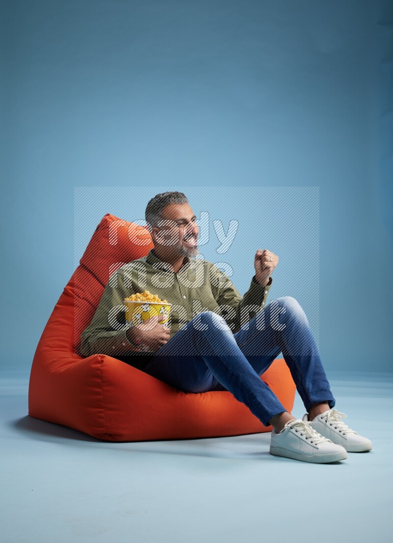 A man sitting on an orange beanbag and eating popcorn