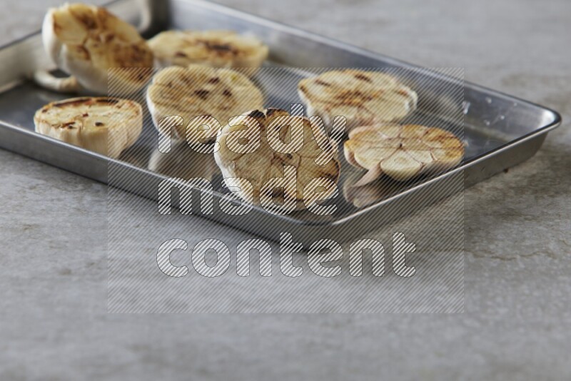 half's roasted garlic in a stainless tray on a grey textured countertop