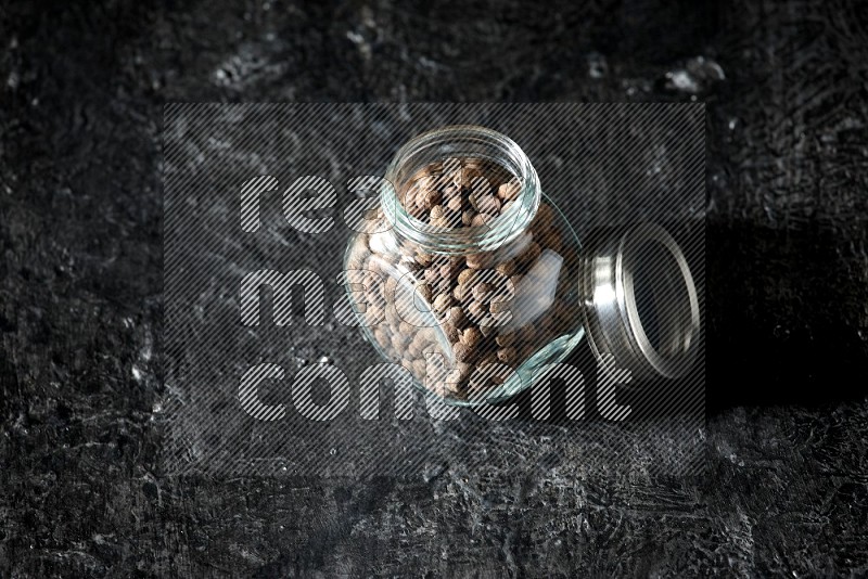 A glass spice jar full of allspice whole balls on a textured black flooring