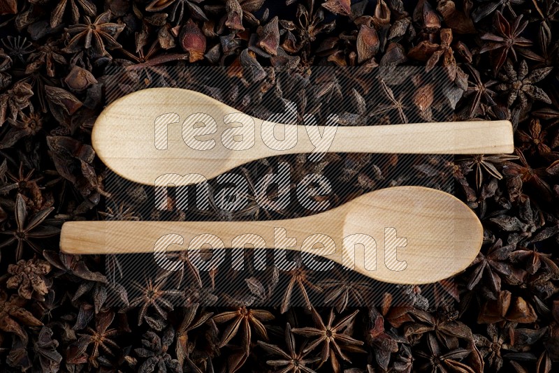 Star anise filling the frame and two empty wooden spoons on it