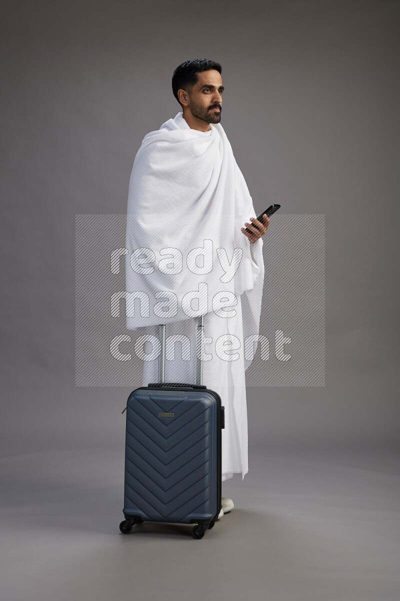 A man wearing Ehram Standing holding traveling bag on gray background