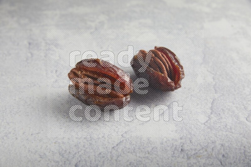 two pecan stuffed madjoul dates on a light grey background