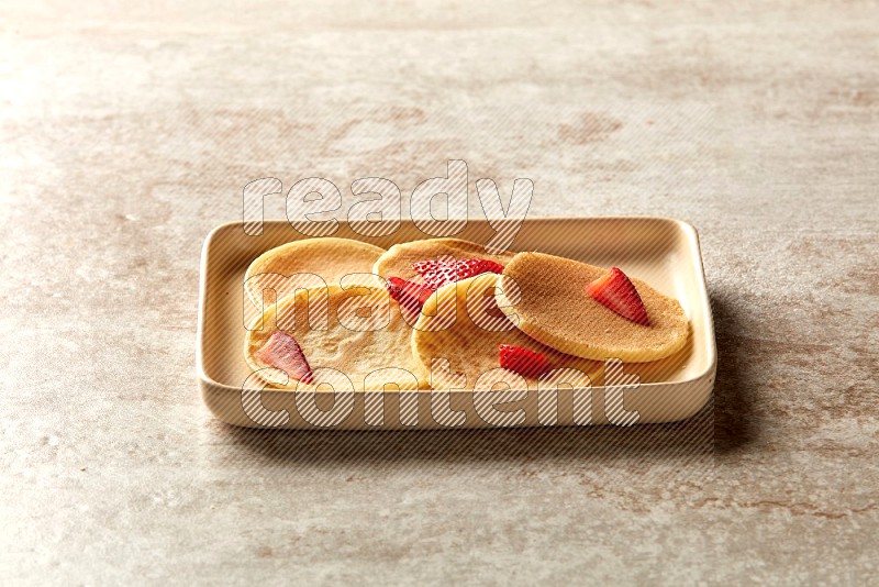 Five stacked strawberry mini pancakes in a rectangular plate on beige background