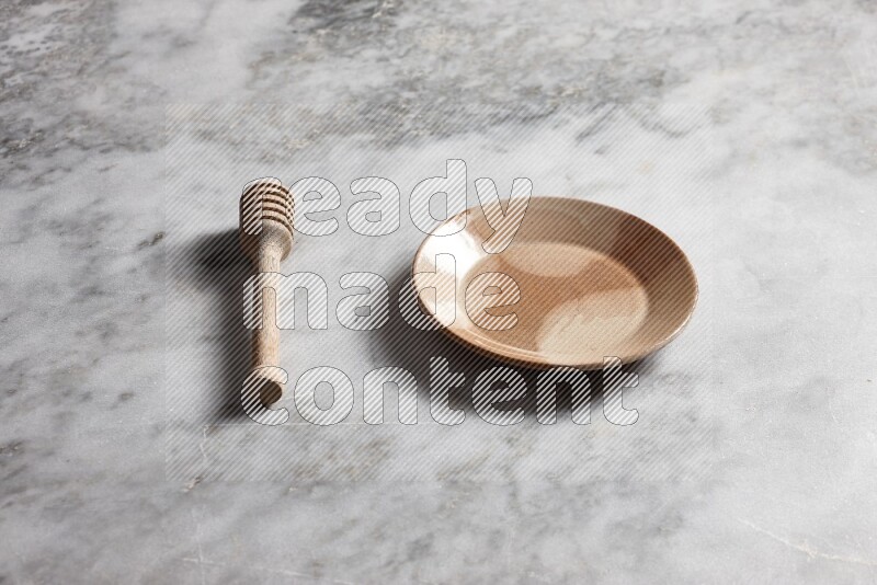 Multicolored pottery plate with wooden honey dipper on the side on grey marble background