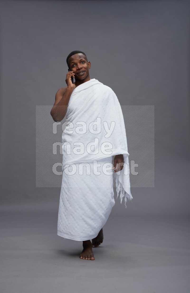 A man wearing Ehram Standing talking on phone on gray background