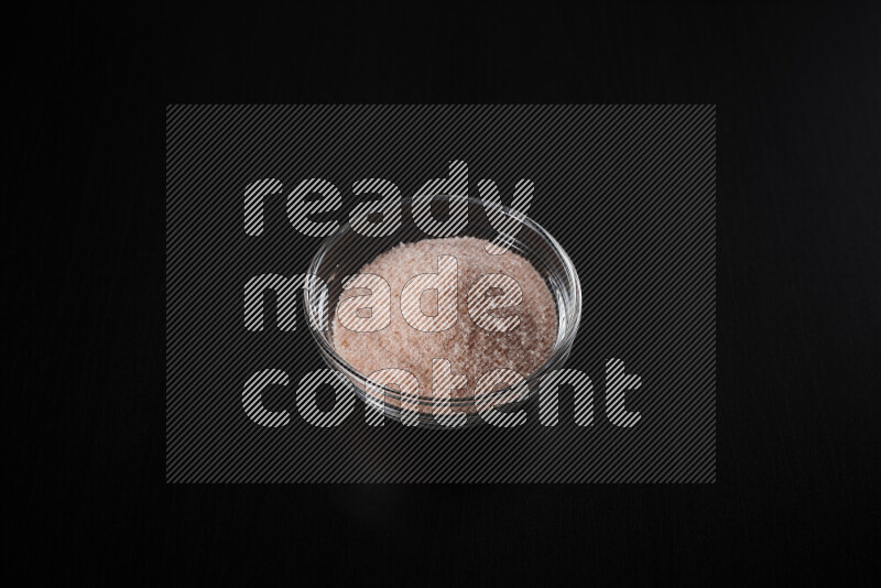 A glass bowl full of fine himalayan salt on black background