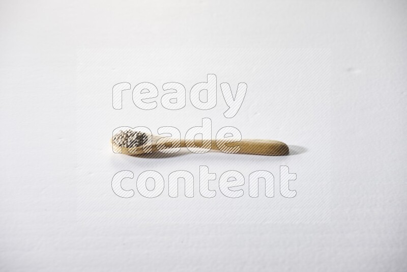 ملعقة خشبية مملوءة بحبوب الفلفل الأبيض على أرضية بيضاء