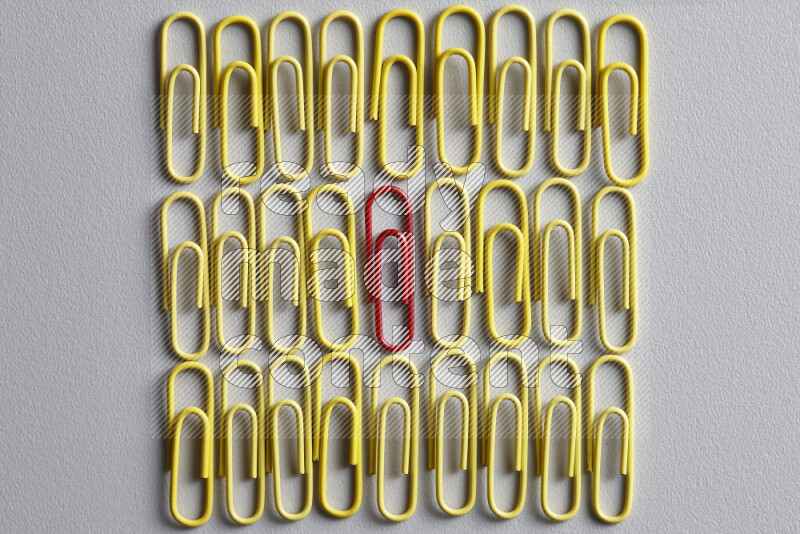 مجموعة من مشابك الورق الصفراء مع مشبك ورق ملون مختلف في المنتصف على خلفية رمادية