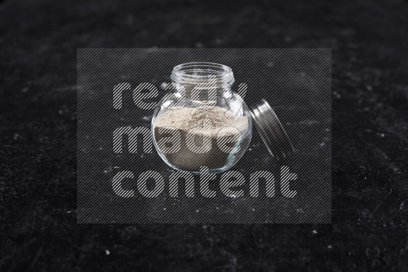 A glass jar full of onion powder on black background