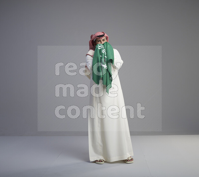 رجل سعودي يرتدي ثوب ابيض وشماغ احمر يقبل علم السعودية