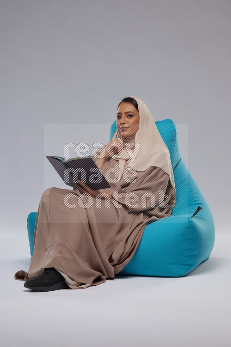 A woman sitting on a blue beanbag and reading a book