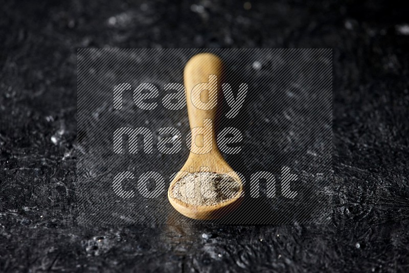 A wooden spoon full of white pepper powder on textured black flooring