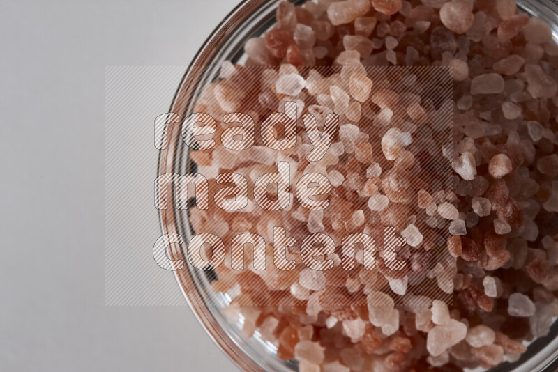 A glass bowl full of coarse himalayan salt crystals on white background