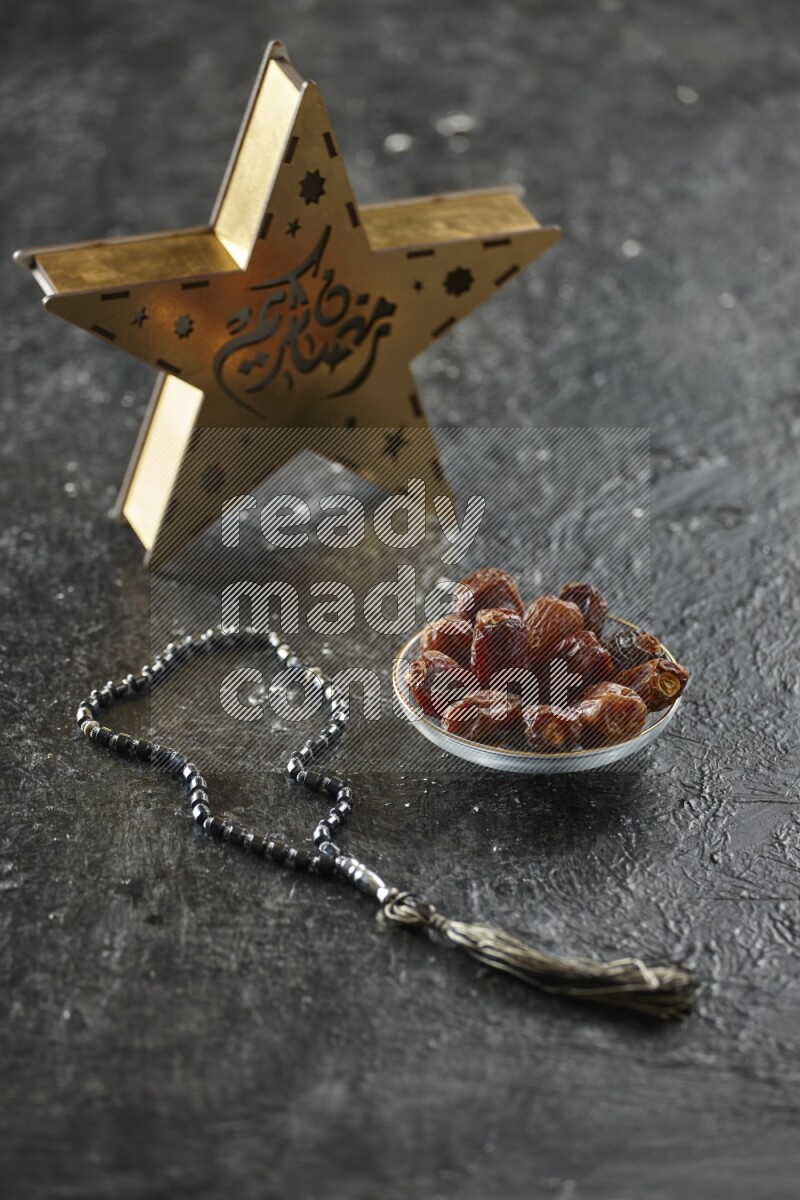 A wooden golden star lantern with different drinks, dates, nuts, prayer beads and quran on textured black background