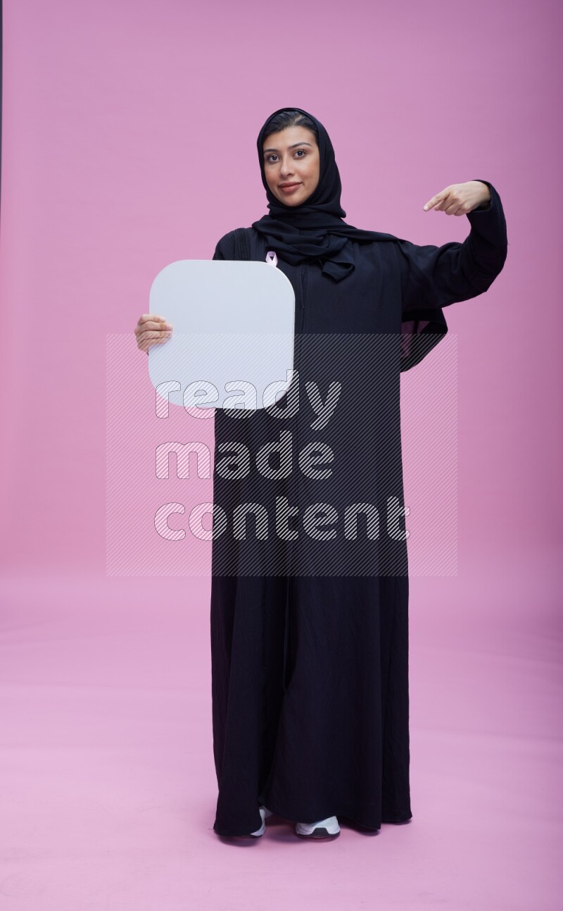 Saudi woman wearing pink ribbon on Abaya standing holding social media signs on pink background