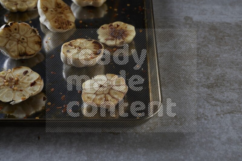 half's roasted garlic in a stainless tray on a grey textured countertop