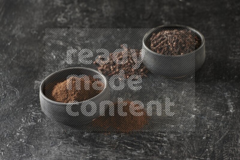 وعاءين من الفخار الأسود أحدهما ممتلئي بحبوب القرنفل والآخر ممتلئ ببودرة القرنفل على خلفية سوداء