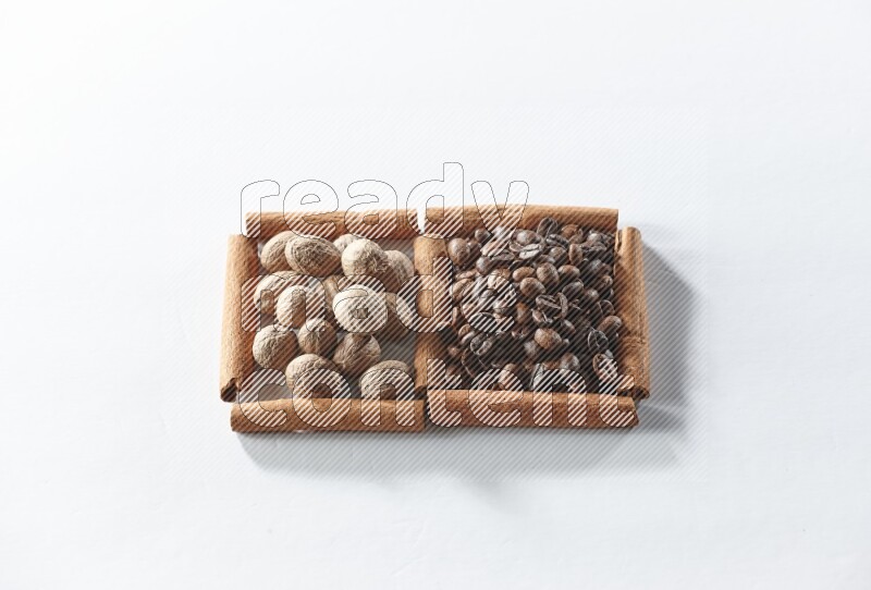 مربعان من أعواد القرفة ممتلئان بحبوب القهوة وجوزة الطيب علي خلفية بيضاء