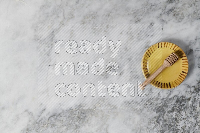 Multicolored pottery plate with wooden honey dipper in it on grey marble background