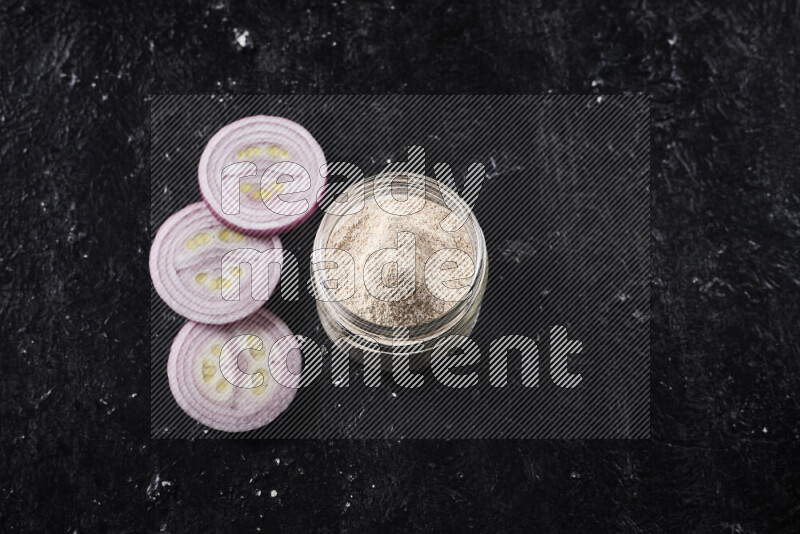 A glass jar full of onion powder on black background