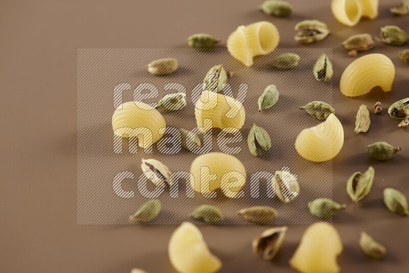 Raw pasta with different ingredients such as cherry tomatoes, garlic, onions, red chilis, black pepper, white pepper, bay laurel leaves, rosemary and cardamom on beige background