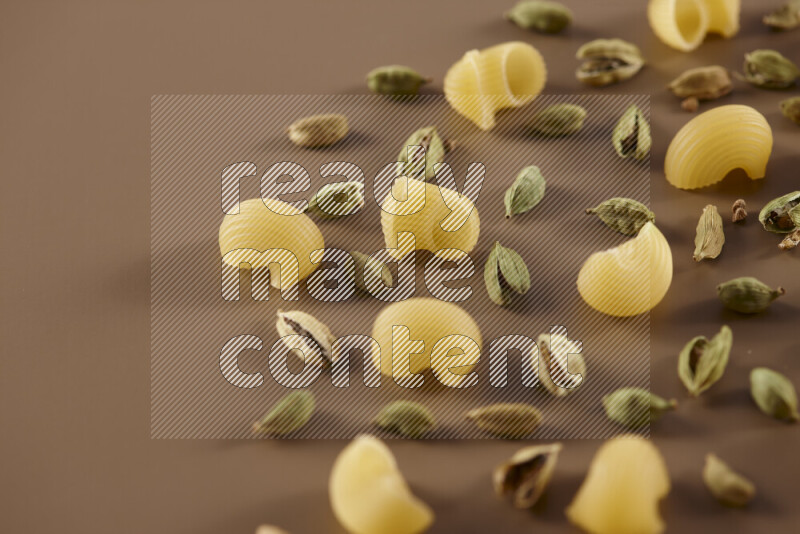 Raw pasta with different ingredients such as cherry tomatoes, garlic, onions, red chilis, black pepper, white pepper, bay laurel leaves, rosemary and cardamom on beige background
