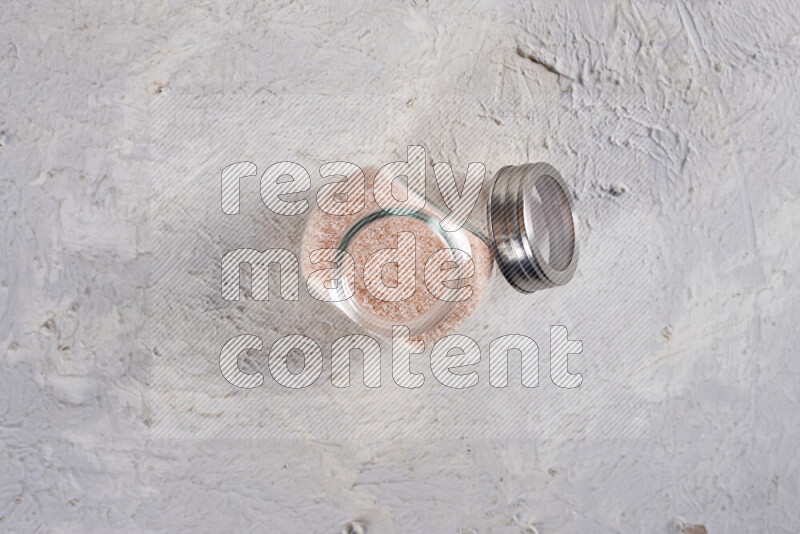 A glass jar full of fine himalayan salt on white background