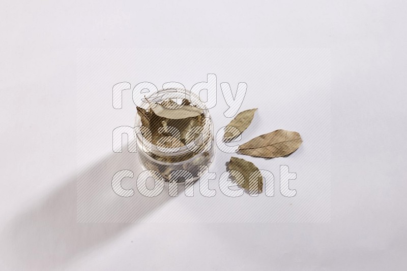 A glass jar filled with dried bay leaves on white flooring