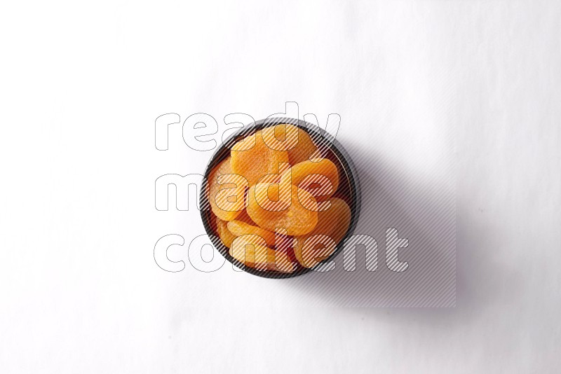 Dried apricots in a black pottery bowl on white background