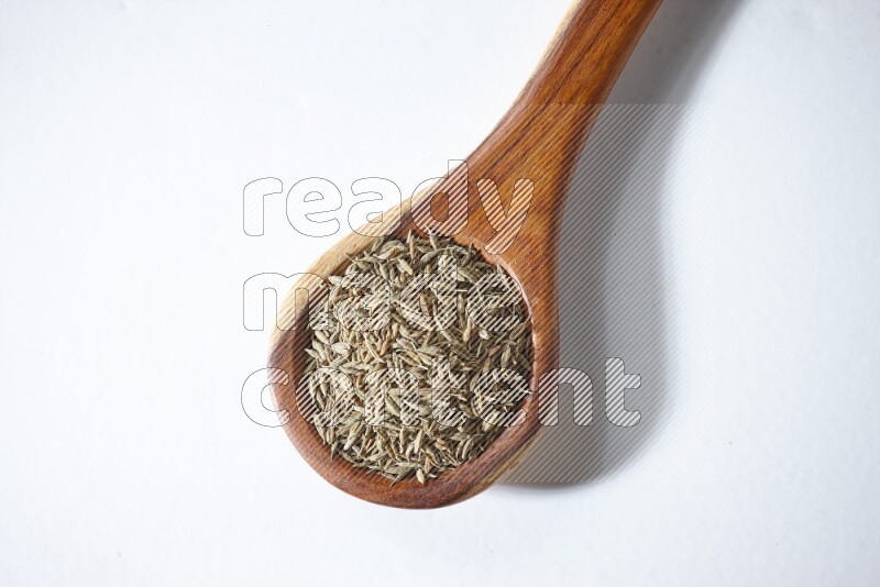 A wooden ladle full of cumin seeds on a white flooring