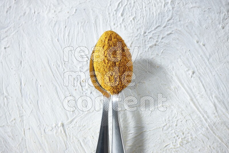 2 metal spoons full of turmeric powder on a textured white background