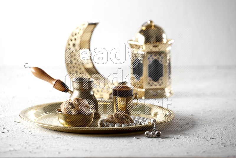Dried figs in a metal bowl with coffee and prayer beads on a tray beside lanterns in a light setup