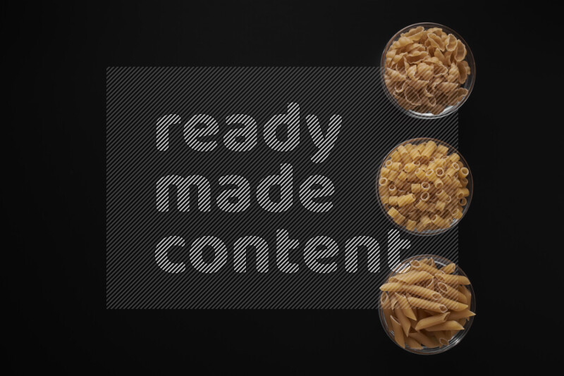 Different pasta types in 3 glass bowls on black background
