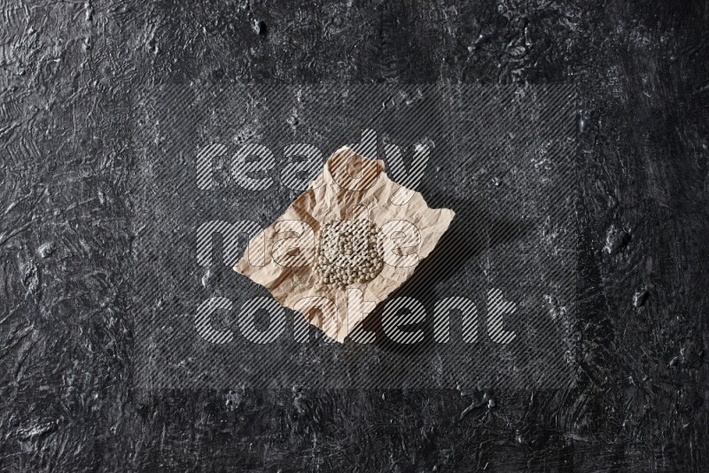 White pepper beads in a crumpled piece of on textured black flooring