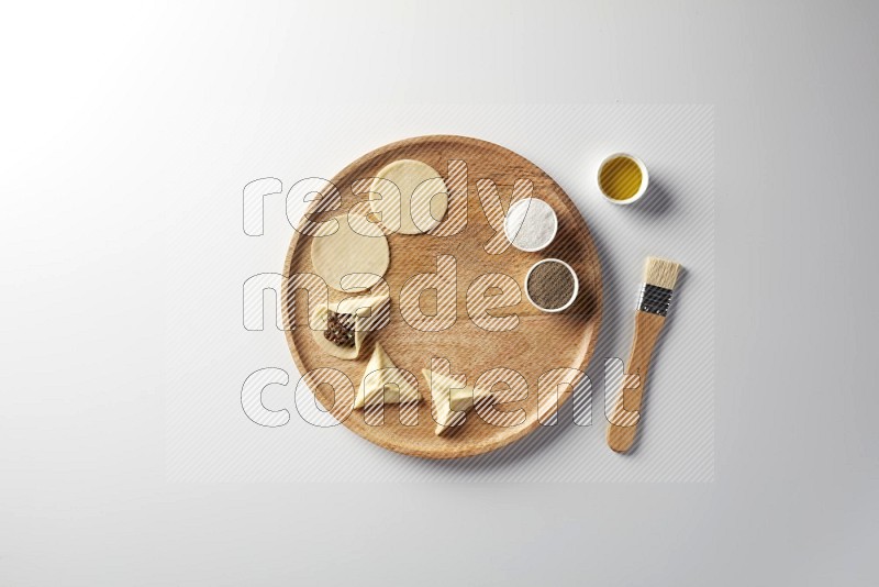 two closed sambosas and one open sambosa filled with meat while salt, black pepper and oil with oil brush aside in a wooden dish on a white background