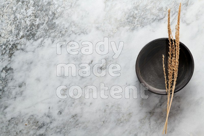 Wheat stalks on Black Pottery Oven Plate on grey marble flooring, Top view