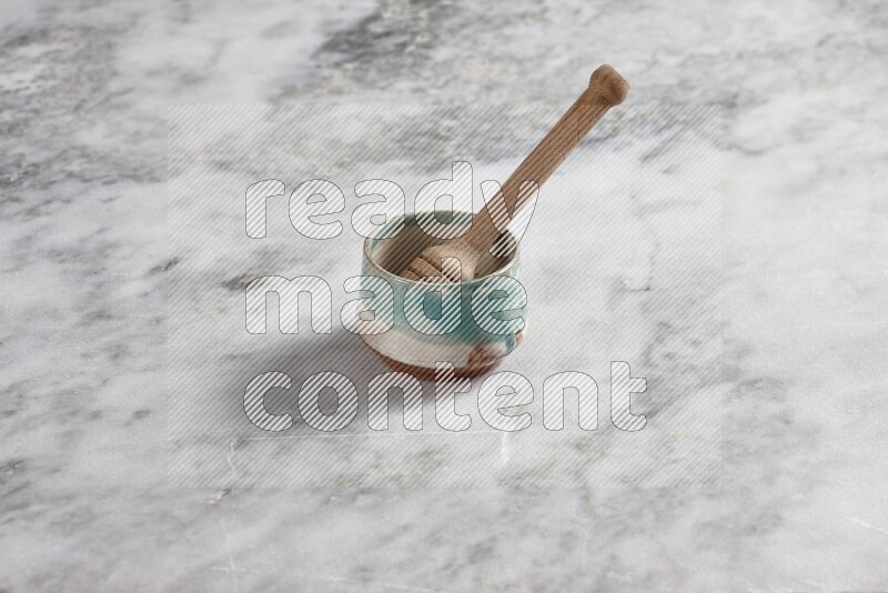 Multicolored pottery bowl with wooden honey dipper in it on grey marble background