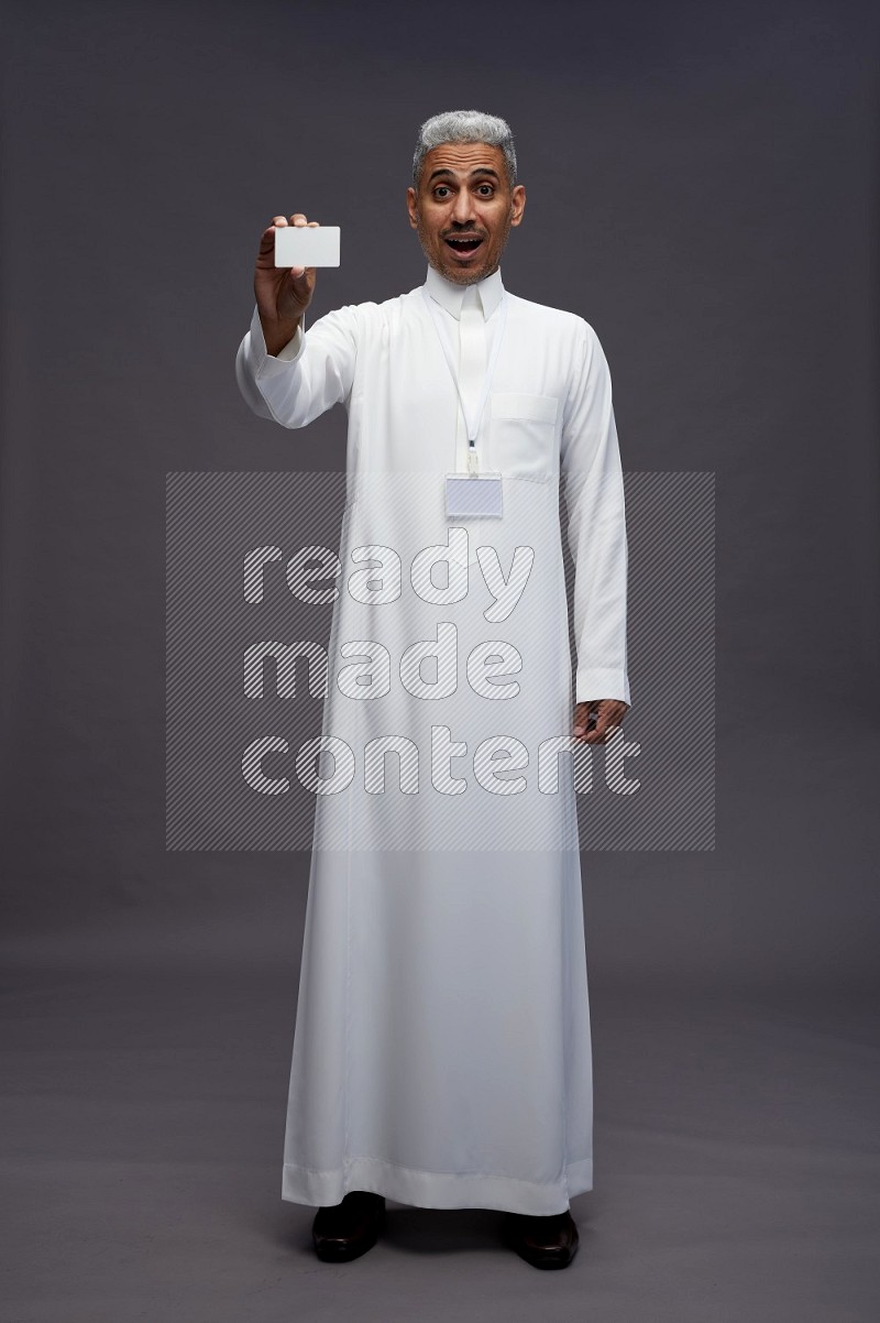 Saudi man wearing thob with neck strap employee badge standing holding ATM card on gray background