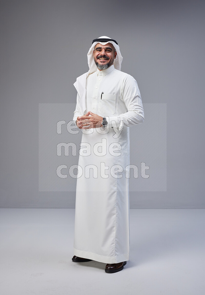 Saudi man Wearing Thob and white Shomag standing interacting with the camera on Gray background