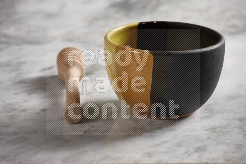 Multicolored pottery bowl with wooden honey dipper on the side on grey marble background